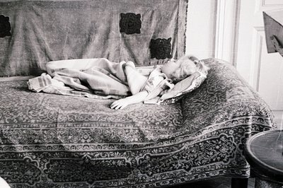 A child rests on an ornate, patterned sofa beneath a decorative textile. The scene suggests a domestic interior, possibly mid...