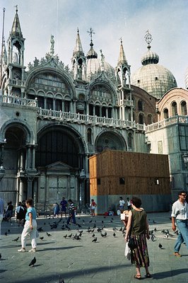St. Mark's Basilica, Venice, with visible scaffolding indicating restoration work. A crowd of tourists, pigeons, and a few lo...