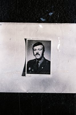Formal portrait of a man in a military uniform, likely 1970s era, with a prominent mustache. The photograph is affixed to a t...