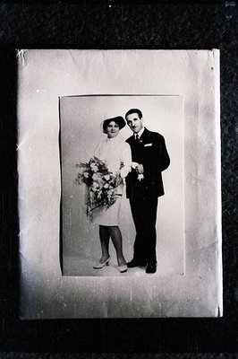 Formal studio portrait of a couple, likely a wedding. The bride wears a short-sleeved dress and carries a bouquet of flowers....