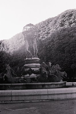 Monumental fountain depicts a muscular male figure holding aloft a tiered structure, surrounded by sculpted horses and water ...