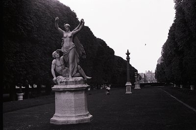 Dramatic neoclassical sculpture of a woman standing triumphantly over a fallen man, atop a stone pedestal. Formal, manicured ...
