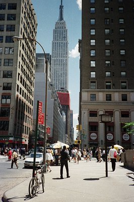 Urban street scene, likely New York City, with the Empire State Building dominating the skyline. Pedestrians and vehicles nav...