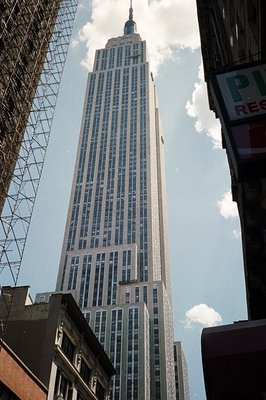 Striking upward view of the Empire State Building, framed by surrounding buildings and a wire grid. The Art Deco skyscraper d...