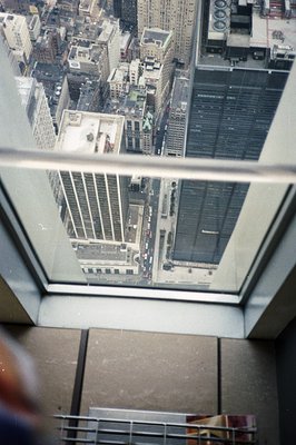 High-angle view through a window shows a cityscape with densely packed buildings and visible street traffic. The frame includ...