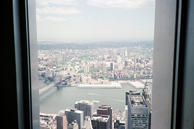 A high-angle view from a skyscraper showcases a dense urban landscape dominated by the East River and a bridge (likely the Ma...