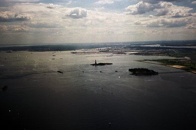 Aerial view of New York Harbor showcasing Liberty Island with the Statue of Liberty, Ellis Island, and extensive shipping tra...