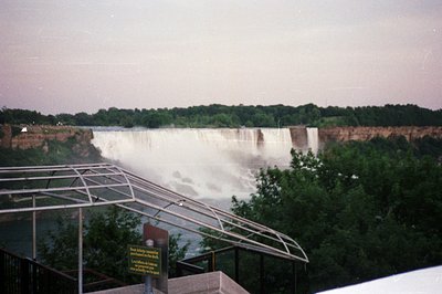 Spectacular view of Niagara Falls, partially obscured by mist. A viewing platform with a modern railing and informational sig...