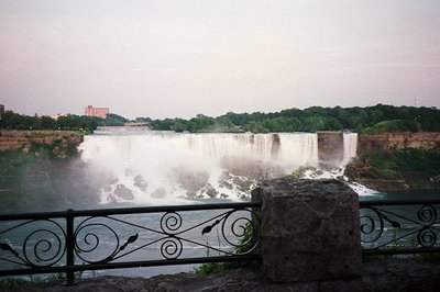 Dramatic view of Niagara Falls, showcasing the powerful cascade of water and misty spray. Lush green trees frame the falls, w...