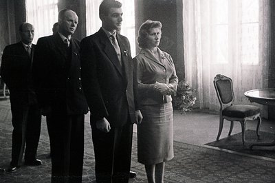 Formal portrait shows three men and one woman in dark suits and a matching skirt set, likely a diplomatic or military gatheri...