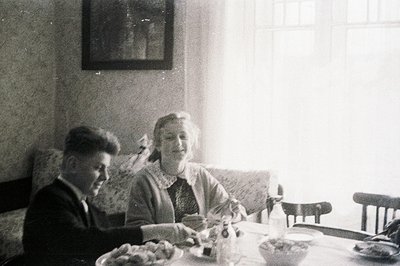 A formal portrait shows a man and woman seated at a table with a decorative tablecloth and dishes. The man wears a suit, and ...