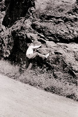 A mid-century man in a suit and dress shoes leaps in a dynamic pose against a rugged, rocky hillside. The rocky terrain with ...