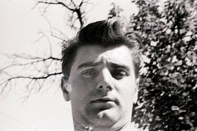 Close-up portrait of a young man with a sharply styled pompadour hairstyle, captured in a low-angle, black-and-white photogra...