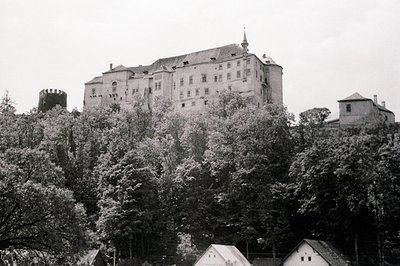Grand Baroque chateau rises above lush foliage. A fortified tower is visible on the left. Likely 18th century, European archi...