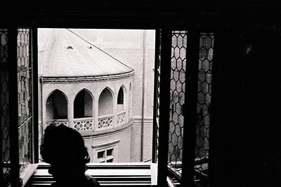 Framed view through a window reveals a building with arched balconies, showcasing architectural details. A figure's silhouett...