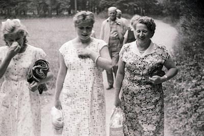 A black and white photo captures a group of people strolling along a path, seemingly in a park setting. Three women in summer...