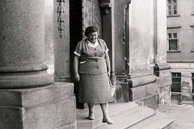 Woman in a tailored suit and skirt descends stone steps, emerging from a building entrance. The architectural details suggest...
