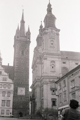 Monumental architecture: A dark stone tower flanks a Baroque church façade with steps leading to the entrance. Note the clock...