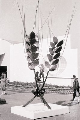 Striking sculpture depicting a wheat stalk with abstract human figures integrated into the design. Likely an exhibition piece...