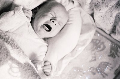 Infant, likely a baby, captured in a distressed cry. Details suggest a candid, possibly home snapshot. The textured blanket a...