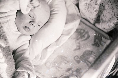A baby sleeps peacefully in a crib covered with a patterned blanket featuring animal illustrations. The monochrome image show...
