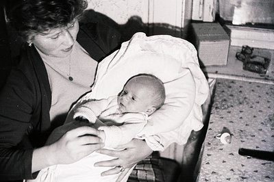 A young woman cradles a newborn baby wrapped in a blanket. Likely a domestic interior scene, with visible patterned flooring ...