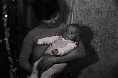A mother cradles an infant in her arms, set against a textured wallpaper backdrop and hinting at a Christmas tree. The image,...