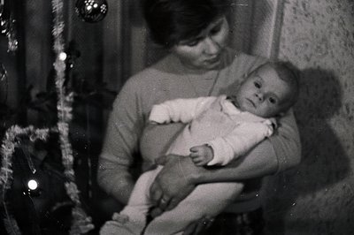 Black and white image depicts a woman holding a baby. The woman wears a turtleneck sweater; the infant is in a white onesie. ...