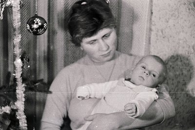 A young woman cradles a baby in her arms, posing near a Christmas tree decorated with a single ornament. A gentle, intimate p...