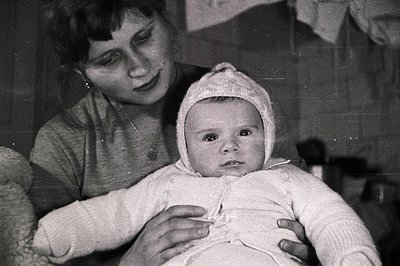 A tender black and white portrait shows a young mother cradling a baby in what appears to be a home setting. The baby wears a...