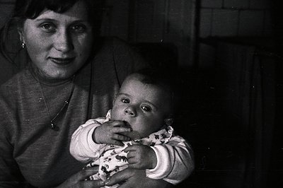 Close-up, monochrome portrait of a woman holding a baby. The woman wears a sweater & necklace; baby in patterned clothing app...