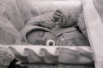 A sleeping infant, swaddled in a knitted blanket and cap, rests within a crib. The scene appears intimate, possibly a persona...