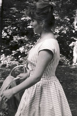 A young woman in a striped dress walks away from the camera, carrying a handled basket. Likely a candid snapshot, exhibiting ...