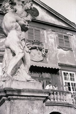 Monumental marble statue of a muscular figure, likely a mythological subject, stands prominently before a weathered, shuttere...