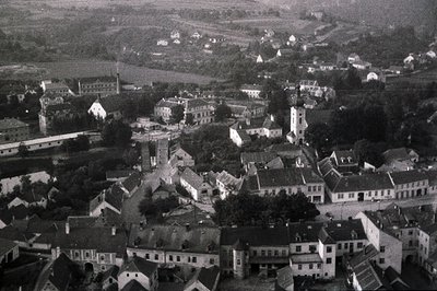 An aerial view captures a compact European town, showcasing tightly packed, gabled buildings and a central church steeple. Th...