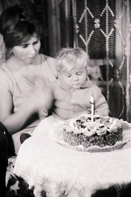 A candid moment captures a young child seated before a cake adorned with cherries and a single candle. The child appears cont...