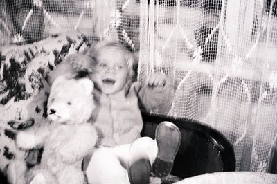 Young child seated in a high chair, clutching a fluffy teddy bear. Likely a family snapshot, showcasing a moment of childhood...