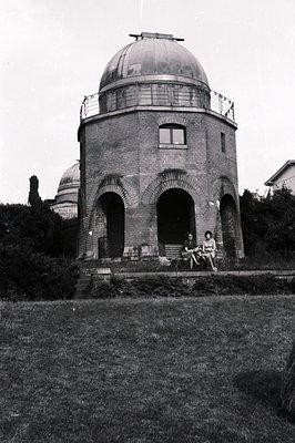 An observatory building with a domed roof sits atop a slight rise. Two women in 1960s attire are seated on a ledge in front. ...