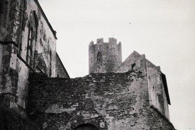 Weathered stone architecture with a crenellated tower rises above a crumbling wall. Textured surfaces suggest age and exposur...