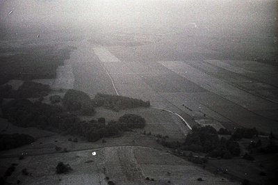 Aerial view showcasing a vast, flat landscape with agricultural fields and scattered tree groupings. A road bisects the scene...