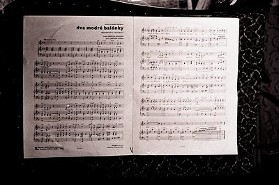 Sheet music titled "dva modré balónky" displayed on an ornate stand. The score features vocal and piano parts, displaying com...