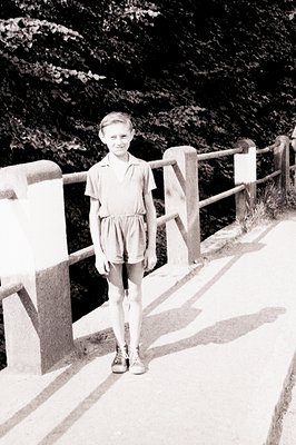 Young boy in a romper suit stands on a bridge with ornate railings, appearing mid-stride. The scene’s dark background suggest...