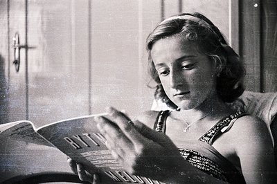 A young woman engrossed in a book, reclined on what appears to be an upholstered chair. She wears a decorative headband and a...