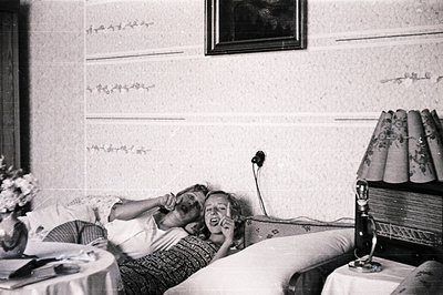 A candid portrait shows two people lounging on a bed, one speaking into a vintage telephone. Floral arrangements and a radio ...