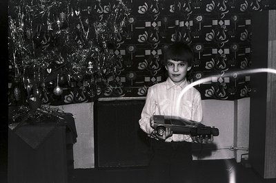 A young boy displays a toy car against a backdrop of a decorated Christmas tree and patterned curtains. The image, likely fro...