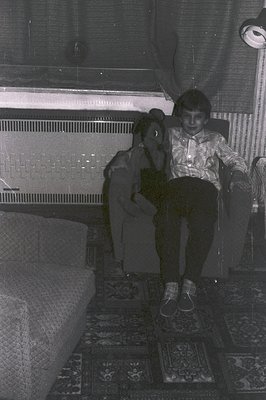 A young boy and girl sit together in a richly patterned room. The boy, wearing a patterned shirt and dark trousers, is seated...