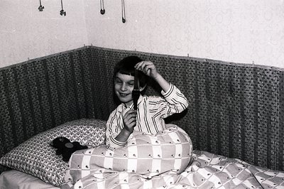 A young girl, likely a child, lies in a bed with a woven headboard. She wears striped pajamas and playfully holds a brush to ...