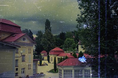 Elegant, multi-story buildings with red tile roofs define a grand courtyard, likely a historic hotel or estate. Lush greenery...