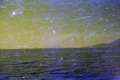 Seascape with gentle waves and distant, low-lying landmass. Heavily scratched/damaged film shows extensive surface wear, indi...