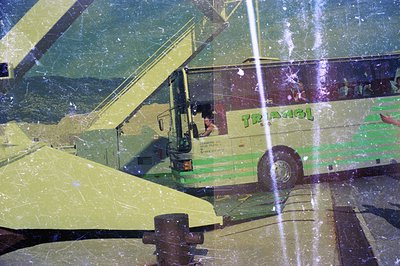 A green “Triangel” tour bus is parked amidst a blurred, sun-drenched landscape; a crane's boom overlaps the scene. Visible te...